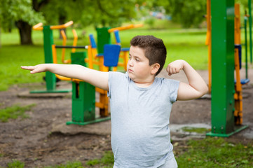 fat boy shows his muscles in background of exercise equipment