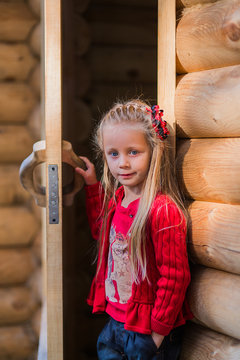 girl with long hair peeping from behind the wooden door of a log house