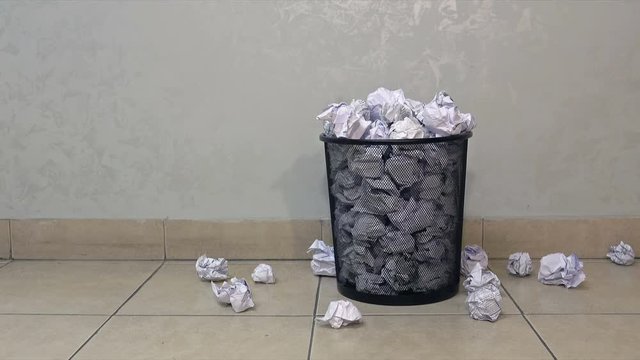 Throwing useless paper into the full waste basket in office. Papers fall on the floor