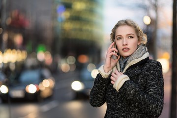 Young blonde and cute woman at phone against out of focused city lights