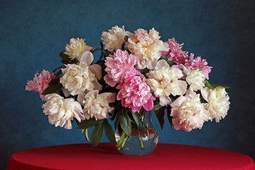 Bouquet of peonies on the table with a red tablecloth.