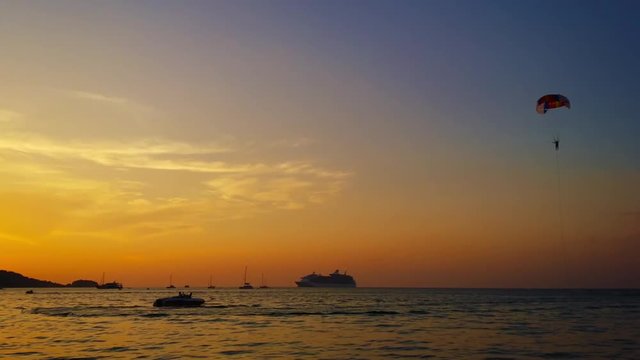 Video 1080p - Adventurous tourist drifting down slowly for a soft, wet landing in the tropical, sea at sunset, after parasailing in  Southeast Asia.
