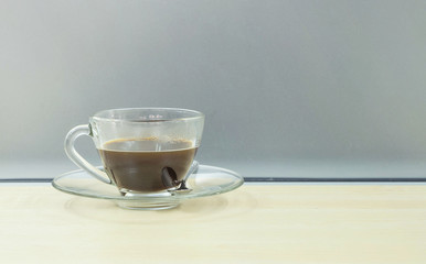Closeup black coffee in transparent cup of coffee on blurred wooden desk and frosted glass wall textured background