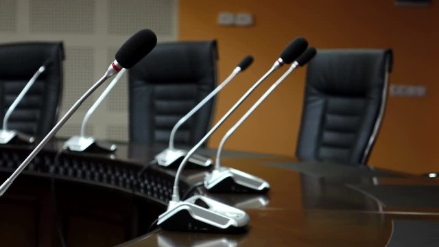 Dolly shot of microphones in modern conference room. Shallow DOF
