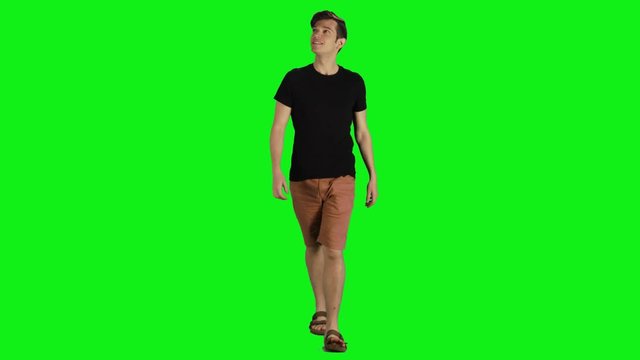 Young man in a full shot walking towards the camera over a green screen. Casual look,  Smiling, looking around, average speed.