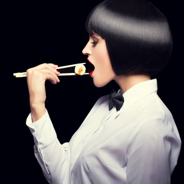 Woman in waiter style eat sushi at night profile view
