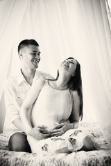 Smiling man hugs his happy pregnant wife sitting on the bed