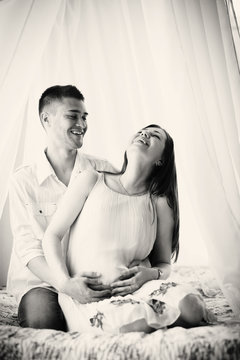 Man hugs his pragnent woman sitting on the bed
