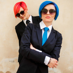 Girls dressed in black suits with blue and pink hair look myster