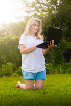 Красивая женщина  на траве в саду с ноутбуком