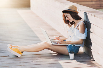 Beautiful hipster girl using laptop outdoors