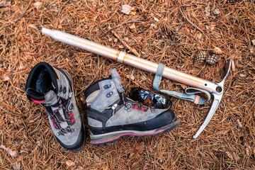 Flat view of hiking boots, sunglasses and ice ax on forest ground