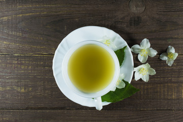 Fototapeta na wymiar A cup of green jasmine tea standing in the center with white jasmine flowers