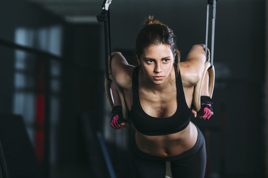 Front view of woman hanging on gymnastic rings at gym