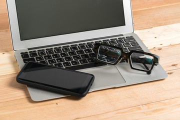 Business workplace from top  smart phone, glasses, laptop on wooden desk