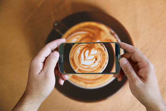 Hand holding smartphone taking photo of coffee. from above,topvi