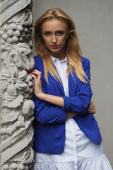 Beautiful young woman in short dress and blue jacket posing near