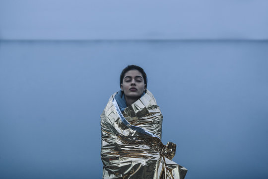 Young woman wrapped in golden plastic standing against lake