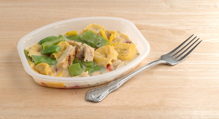 Chicken and tortellini TV dinner with a fork on a wood table top.