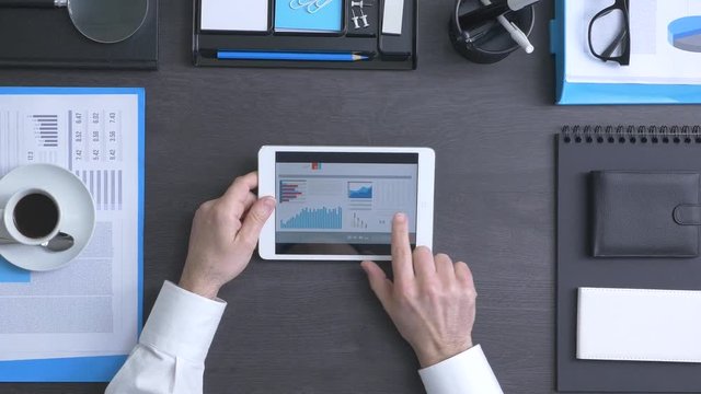 Businessman working at office desk and using a touch screen tablet, he is checking financial reports and using mobile apps