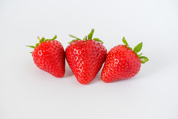 Cluster of ripe red whole fresh strawberries with green stalks and flower buds on a light grey background with