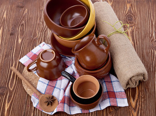 Stack of crockery on wooden table with anise and linen dish-cloth. Set of pottery kitchenware. Buffet, restaurant equipment. Empty plates and cups.
