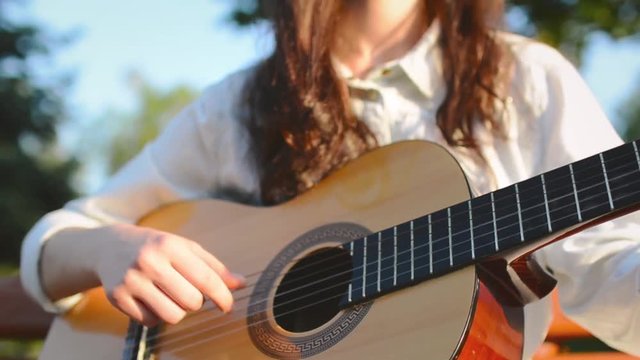 Young Cute Girl Plays on Guitar and Sings  on the bench in the City Park 