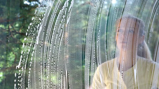 Frustrated, tired woman washes a window with the help of special brushes and sponges. Dolly shot.