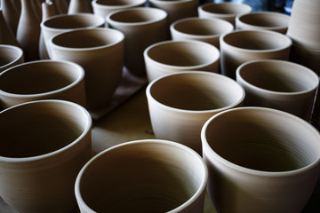 Many rustic handmade terracotta clay pots ready to be fired. Shallow depth of field. Selective focus.