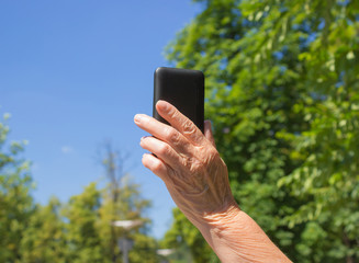 The phone in hand of old woman on the blue sky background