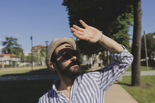 Young man with hat and sunglasses shielding his eyes