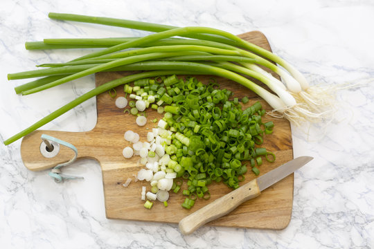 Chopped and whole spring onions on wooden board