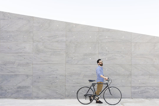 Young man with bicycle in front of grey wall