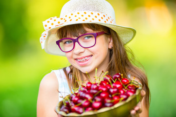 Child with cherries. Little girl with fresh cherries. Young cute caucasian blond girl wearing teeth braces and glasses. Portrait of a smiling young girl with bowl full of fresh cherries.