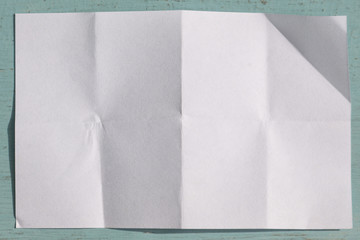 Page of White paper folded and wrinkled on blue wooden background with shadow