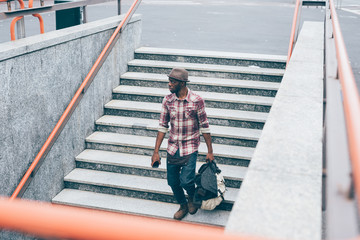 Obraz premium Young handsome afro black man going downstairs to the underground, holding a bag and smartphone, overlooking left - youth, transport concept