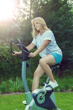 Красивая блондинка занимается спортом на велотренажере в саду