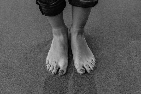 Pies de mujer con u&ntilde;as pintadas sobre la arena de la playa. Fotograf&iacute;a en blanco y negro
