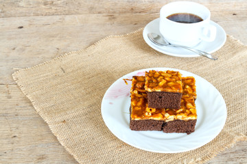Toffee cake garnish with cashew and hot coffee on wooden table.