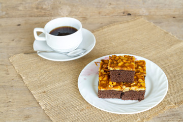 Toffee cake garnish with cashew and hot coffee on wooden table.