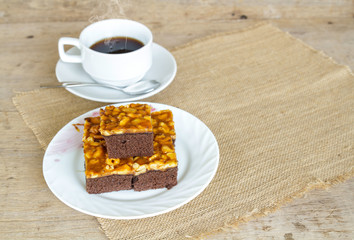 Toffee cake garnish with cashew and hot coffee on wooden table.