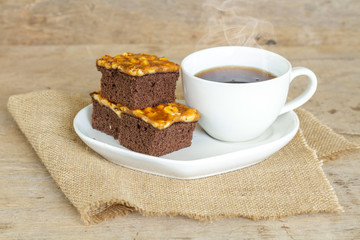 Toffee cake garnish with cashew and hot coffee on wooden table.