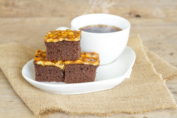 Toffee cake garnish with cashew and hot coffee on wooden table.