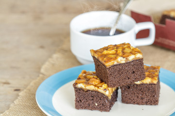 Toffee cake garnish with cashew and hot coffee on wooden table.
