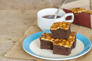 Toffee cake garnish with cashew and hot coffee on wooden table.