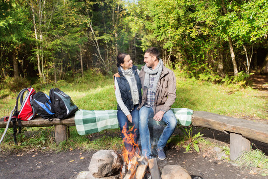 happy couple sitting on bench near camp fire