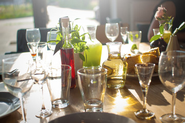 A table with drinks, glasses and goblets standing on a wooden table in a restaurant lit by the afternoon sun