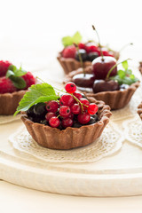 Close up of chocolate tartlets with chocolate cream, fresh strawberries, raspberries, blueberries, red currants and cherries on white wooden background. Selective focus