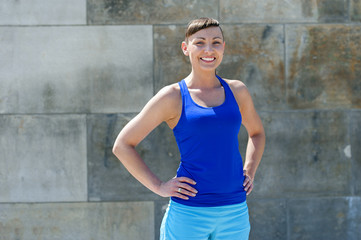 Fit woman smiling. Resting after run against the city wall.