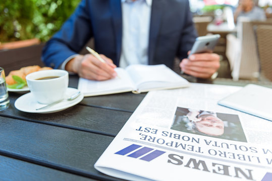 Successful businessman writing in notebook in cafe